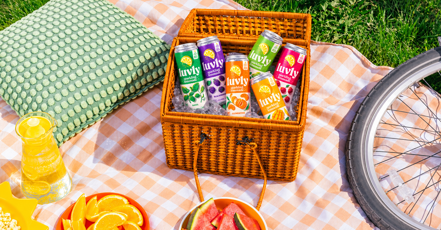 LUVLY sparkling lemonades in a picnic basket with fresh fruit and a bicycle on a sunny afternoon